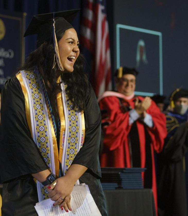 female student on commencement stage smiling at the crowd